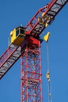 Close-up of a red tower crane operating under a clear blue sky, ideal for construction themes.